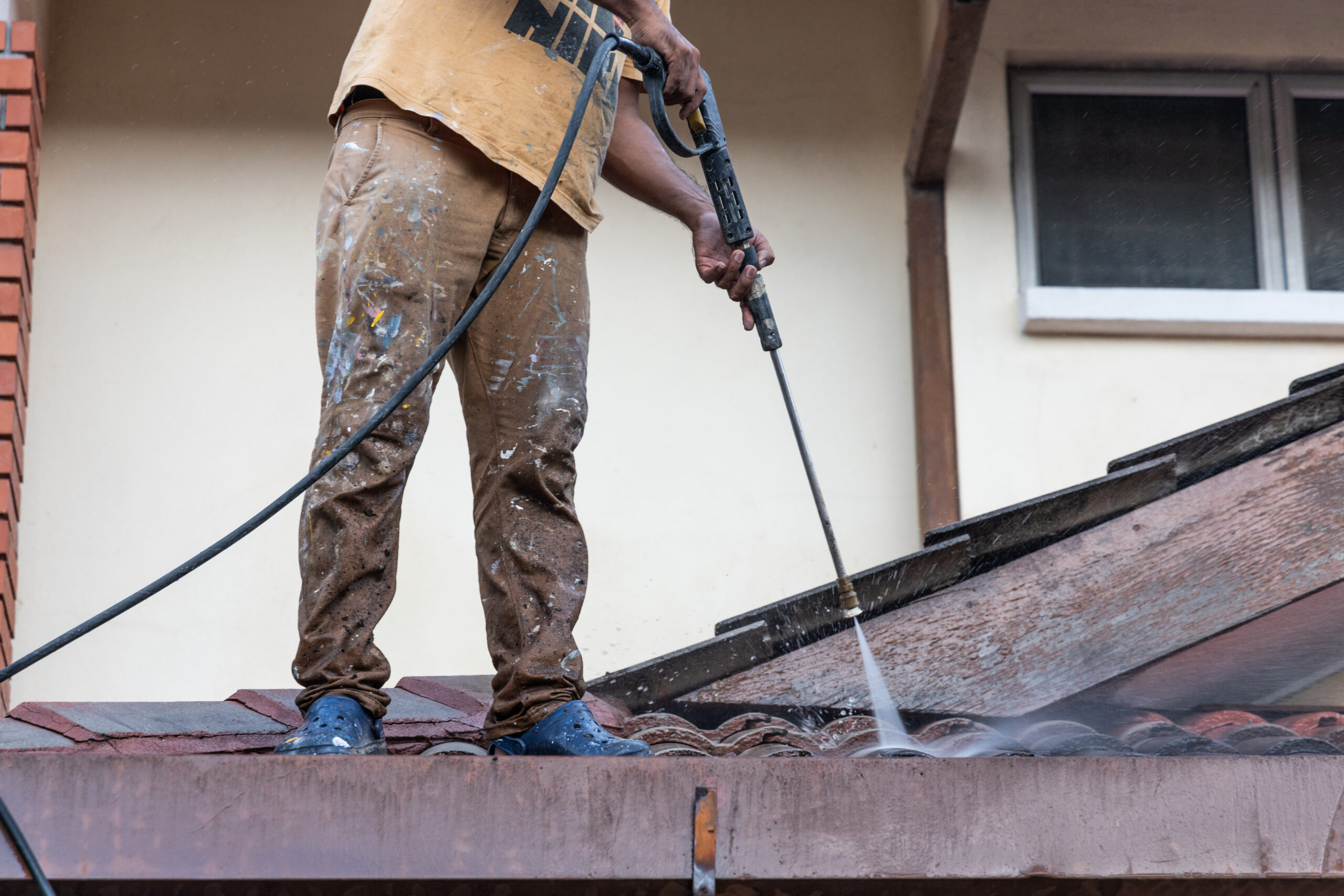 Worker using high pressure water jet spray gun to wash and clean dirt from rooftop tiles in renovation